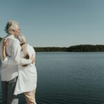 an elderly couple hugging near the lake