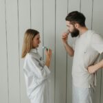 man and woman standing beside white wall while brushing their teeth