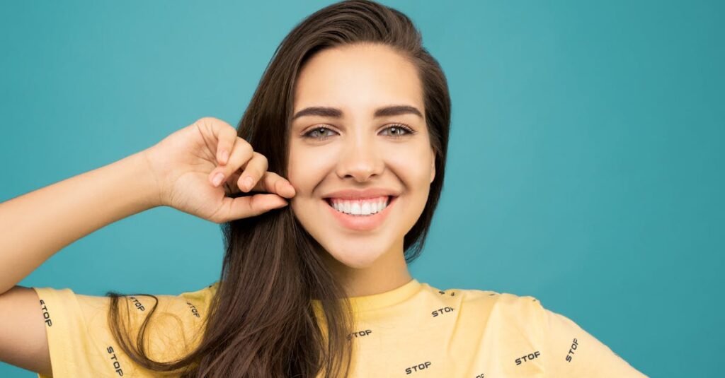 Cheerful young woman smiling brightly against an aqua background.
